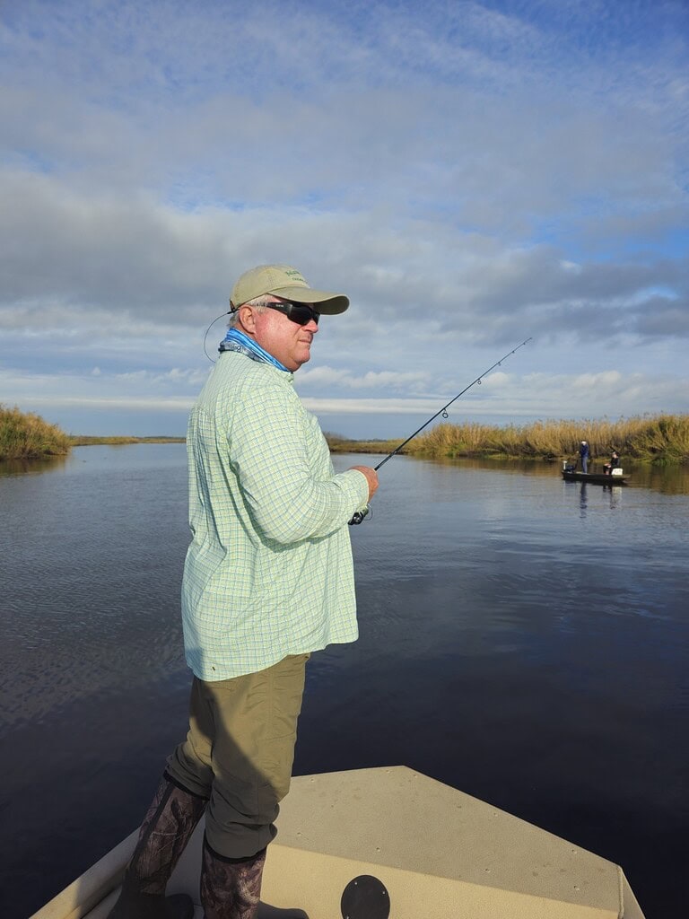 Man fishing on river with fly rod, scenic outdoor setting, blue sky and clouds, fishing trip.