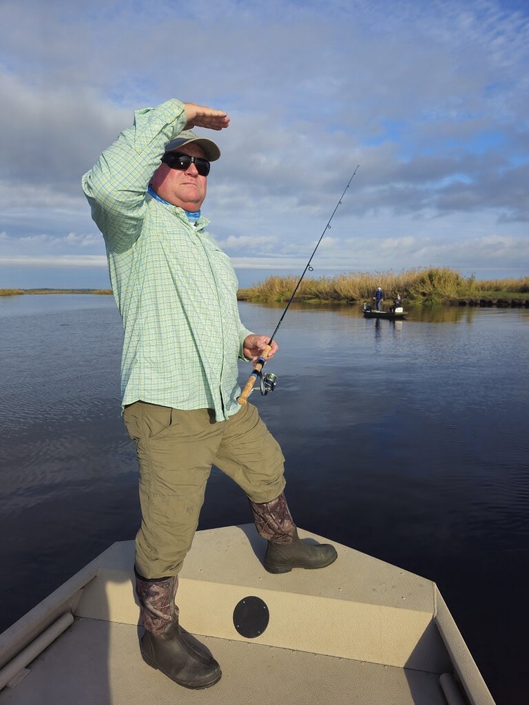 Angler on boat casting with water and sky background.