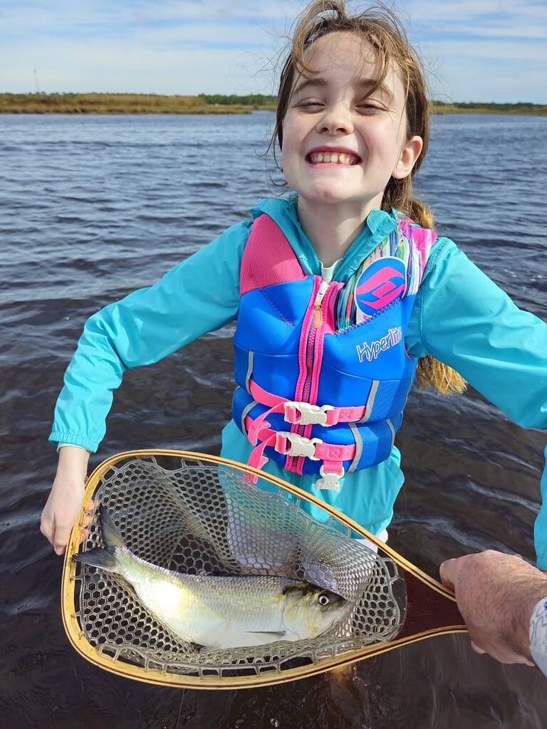 Girl holding fish in net, smiling with catch of American Shad, fly fishing adventure.