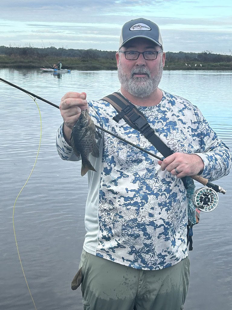 Bluegill caught on a fly fishing rod in a scenic river setting.